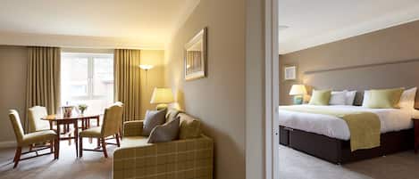 A hotel room with a bed, a sofa, a dining table with chairs, and a lamp.