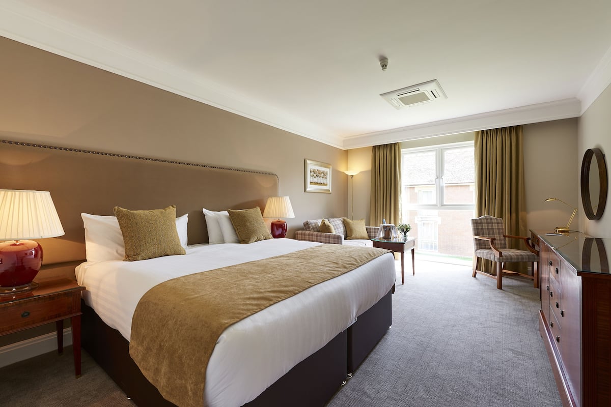 A hotel room with a large bed, a desk, a chair, and a dresser.
