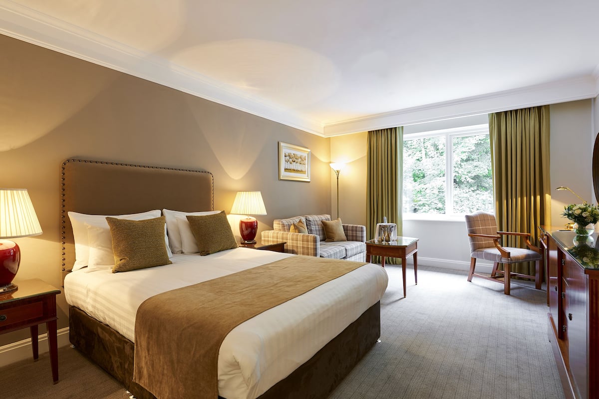 A hotel room with a large bed, a sofa, a chair, a desk, and a window with curtains.