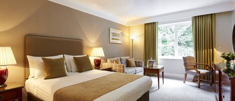 A hotel room with a large bed, a sofa, a chair, a desk, and a window with curtains.