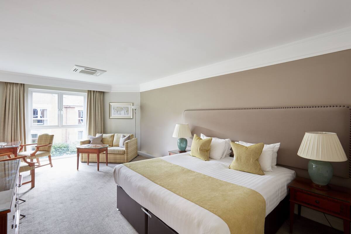 Ein Hotelzimmer mit einem großen Bett, zwei Nachttischen mit Lampen, einem Sofa, einem Schreibtisch und einem Sessel.