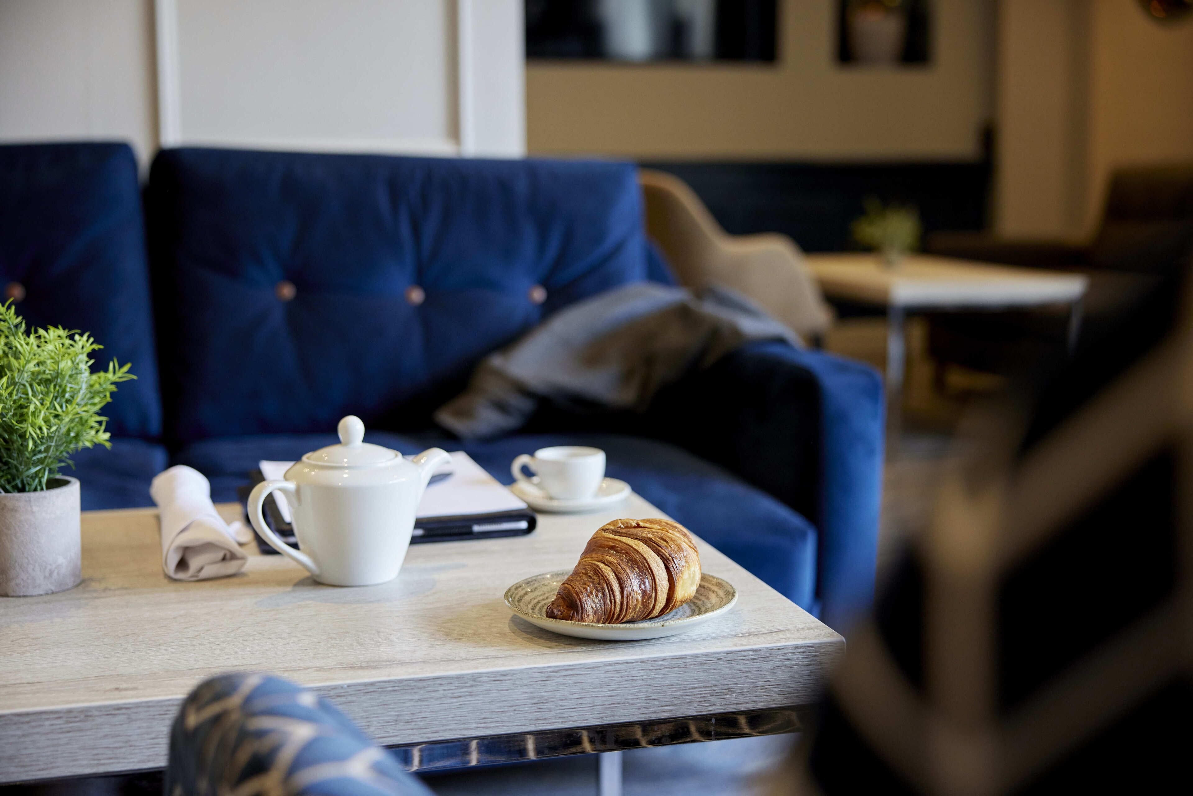 Ein gemütlicher Sitzbereich mit Tisch, einem Croissant, einer Tasse und einem Teekessel.