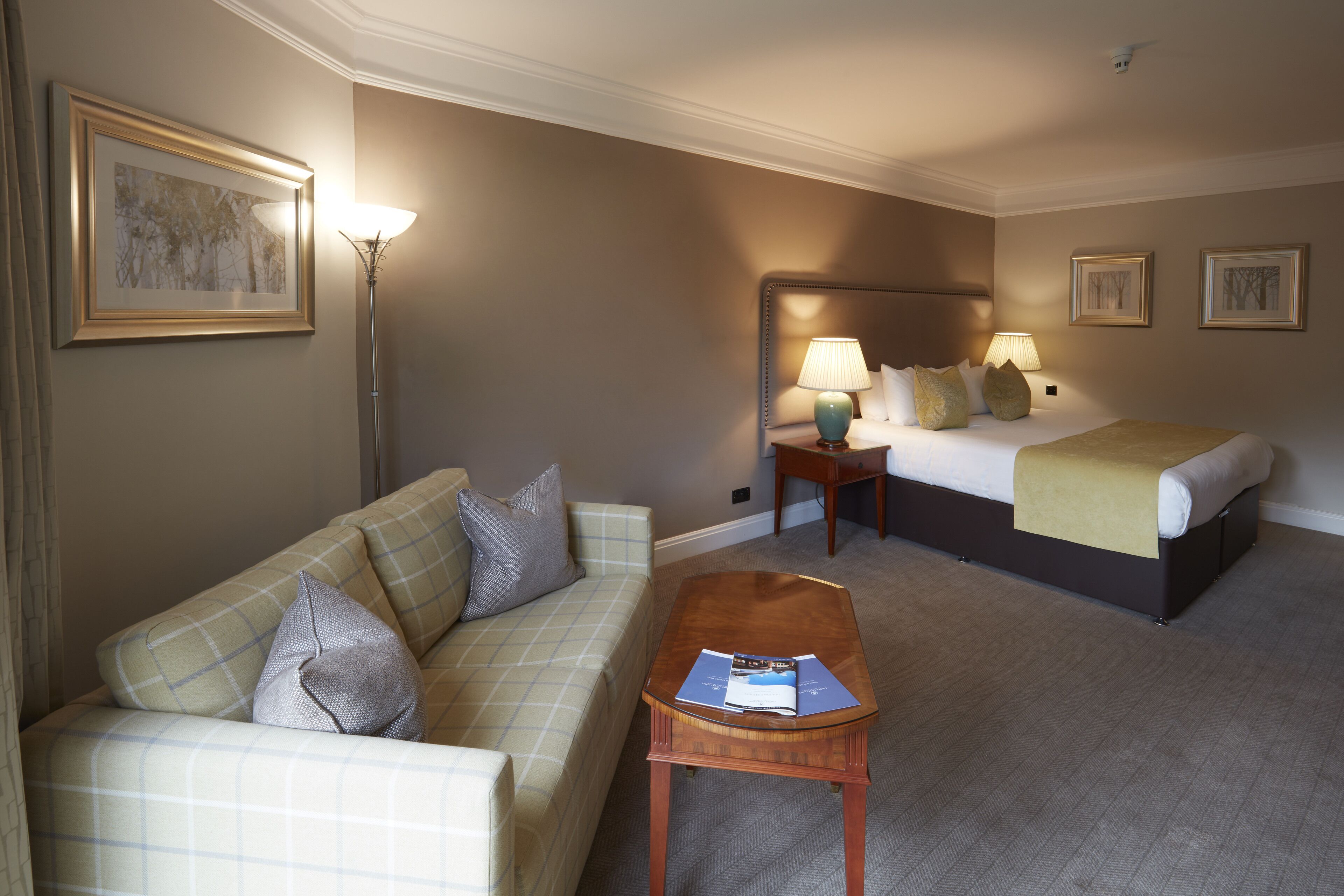 A hotel room with a bed, a sofa, a coffee table, and a lamp.
