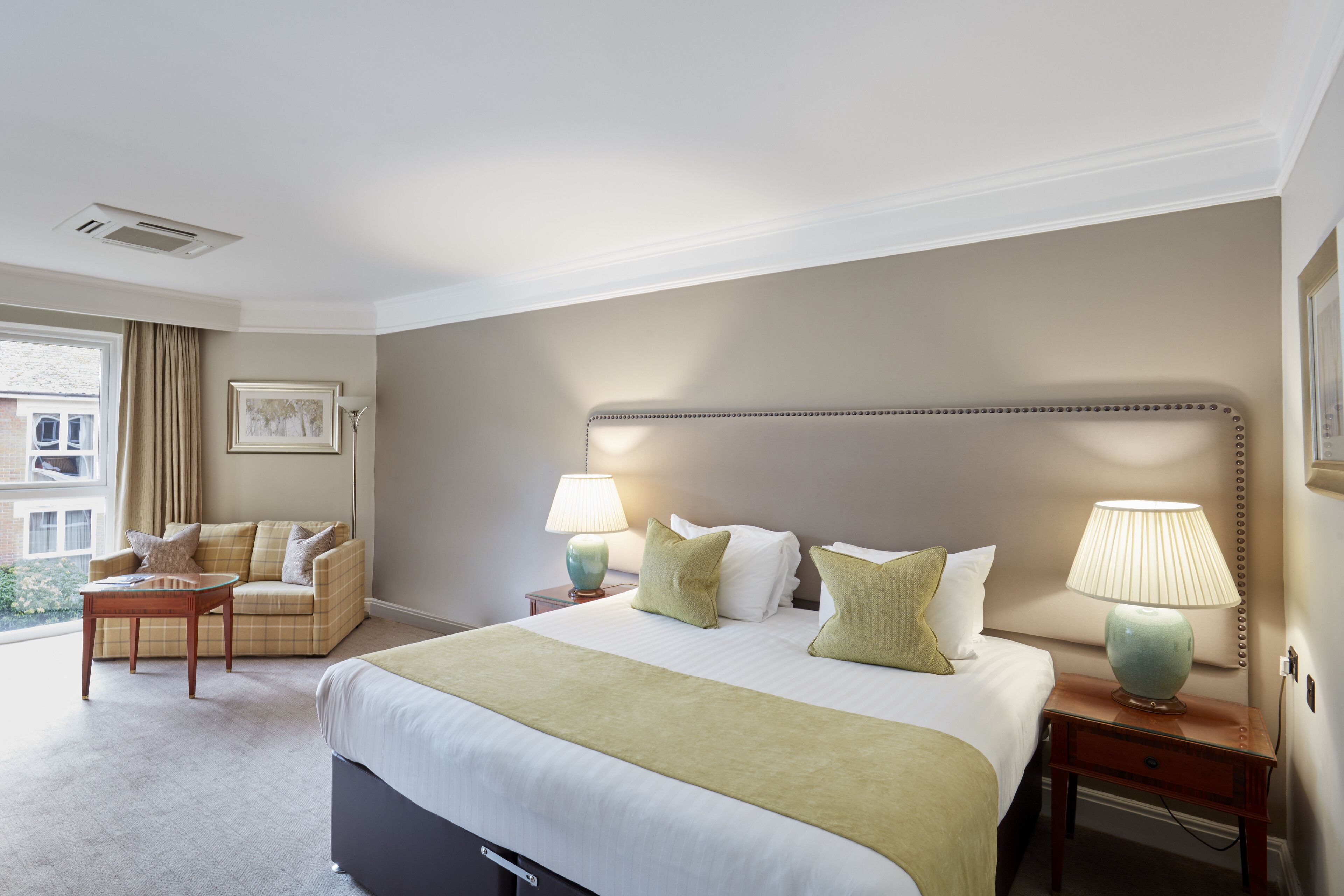 A hotel room with a large bed, two bedside tables with lamps, a sofa, and a window with curtains.