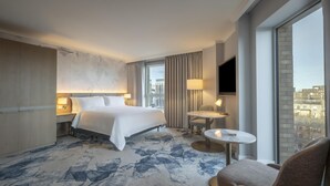 A hotel room with a large bed, a small round table, a chair, a TV, and a window with a city view. - Hilton Dublin (Dublin)