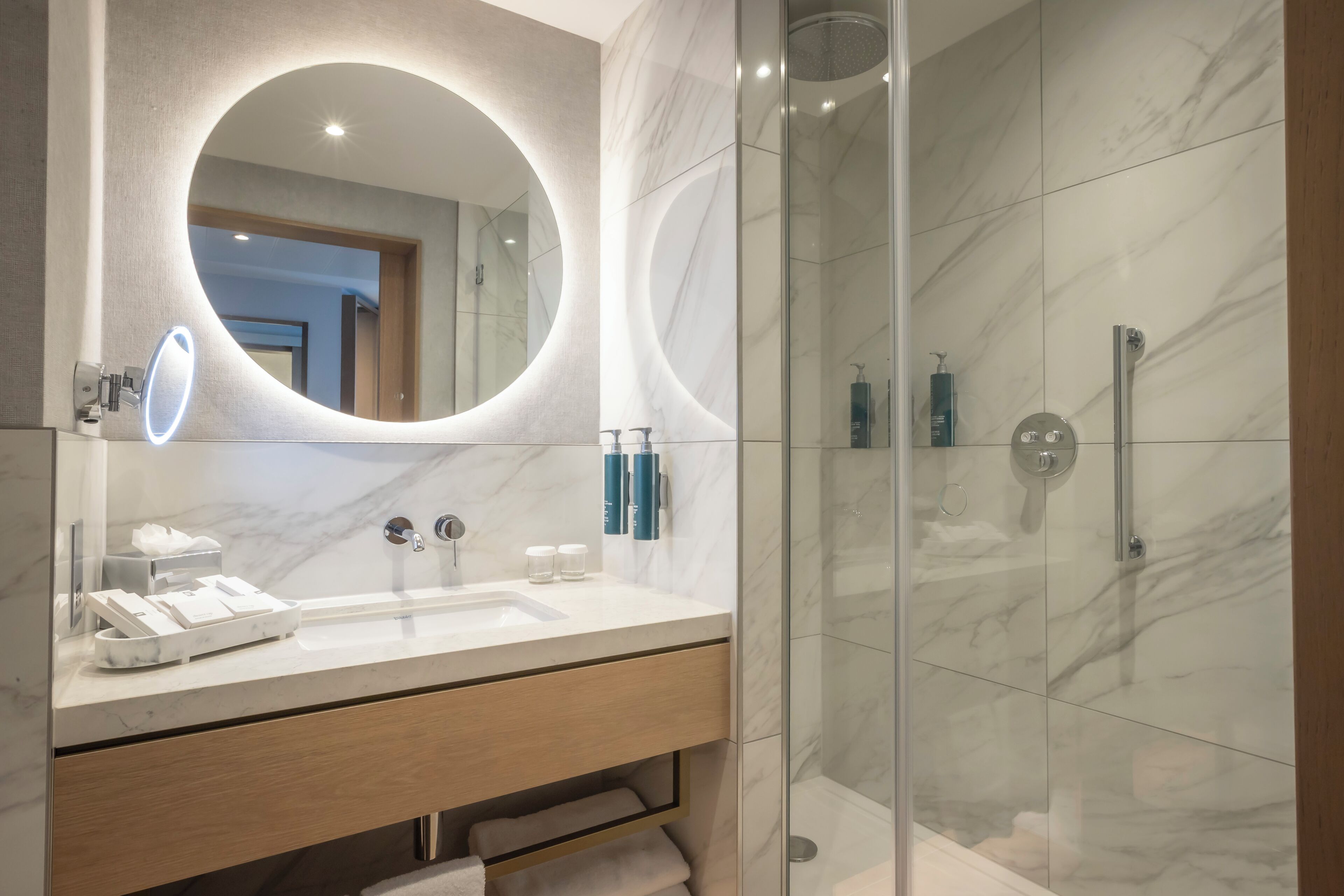 Un baño moderno con lavamanos de mármol, un espejo grande y una ducha con mampara de vidrio.