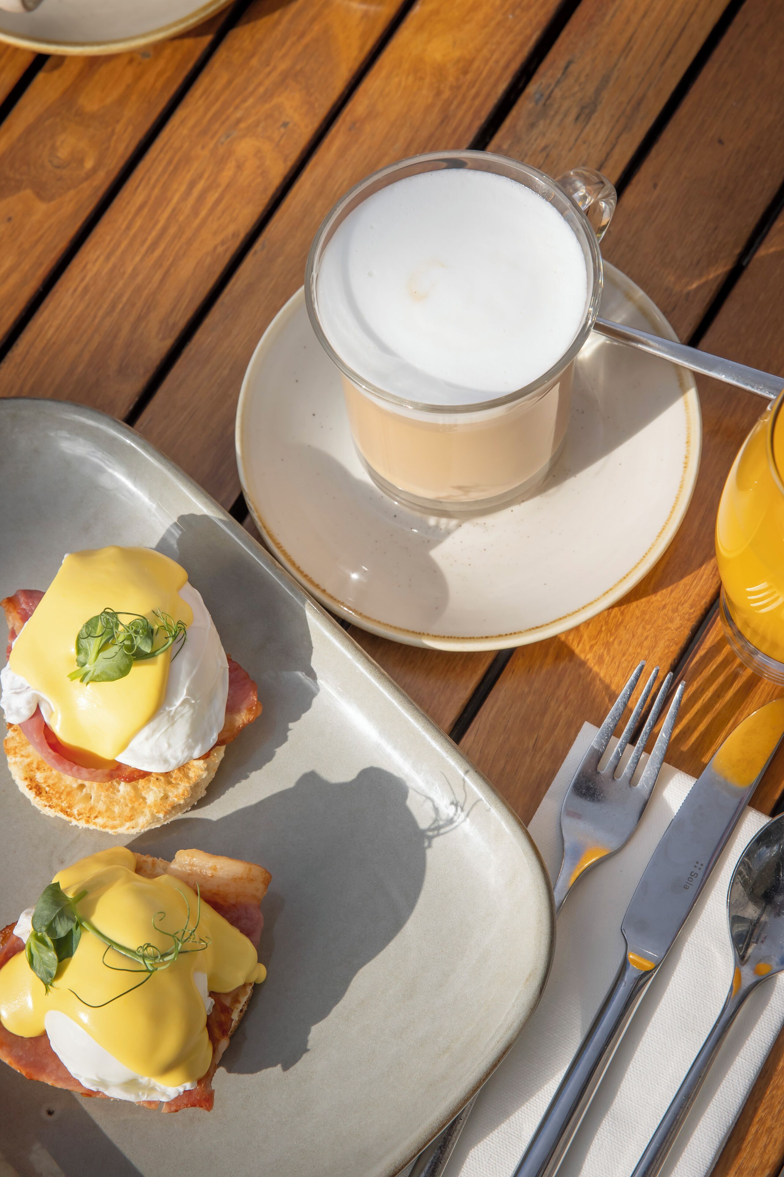 A breakfast setting with eggs Benedict, a cup of coffee, and a glass of orange juice on a wooden table.