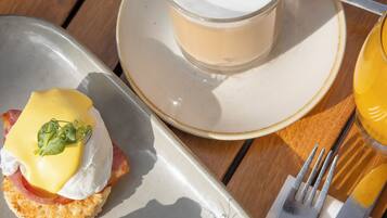 A breakfast setting with eggs Benedict, a cup of coffee, and a glass of orange juice on a wooden table.