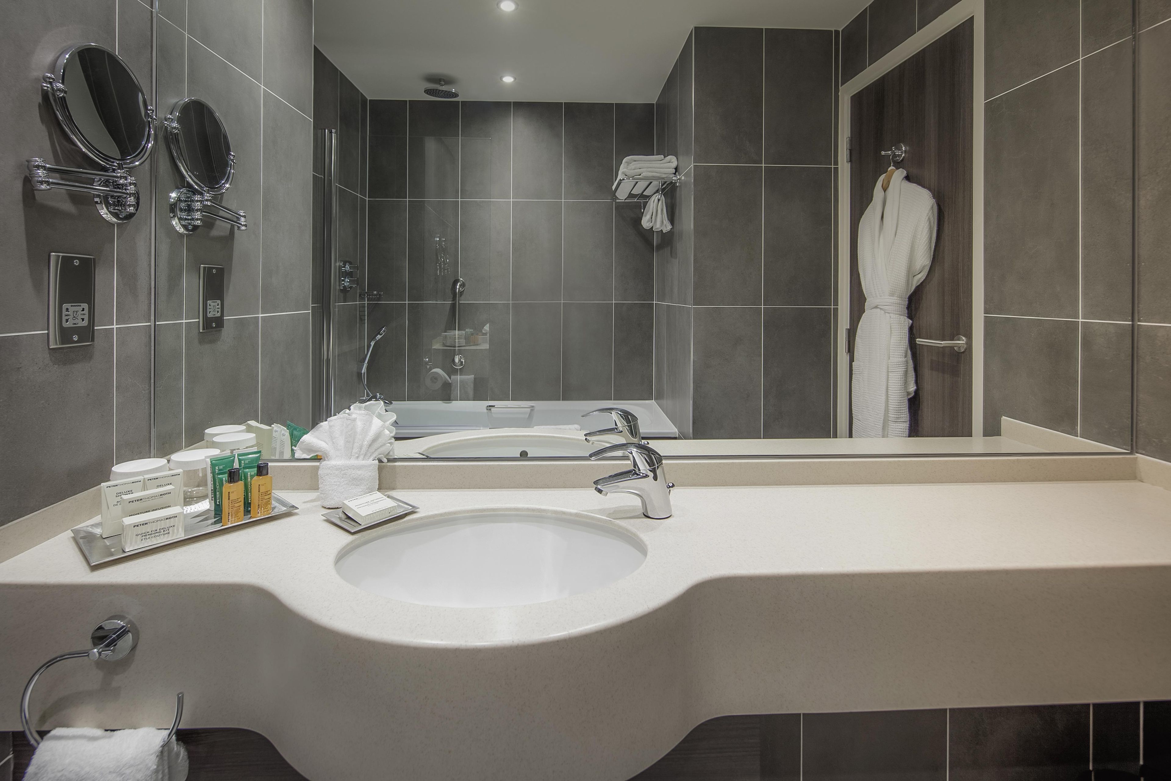 A modern bathroom with a large sink, two mirrors, a shower, and a robe rack.