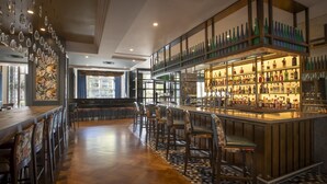 A bar area with a long counter, multiple stools, and a variety of bottles and glasses on shelves. - Hilton Dublin (Dublin)