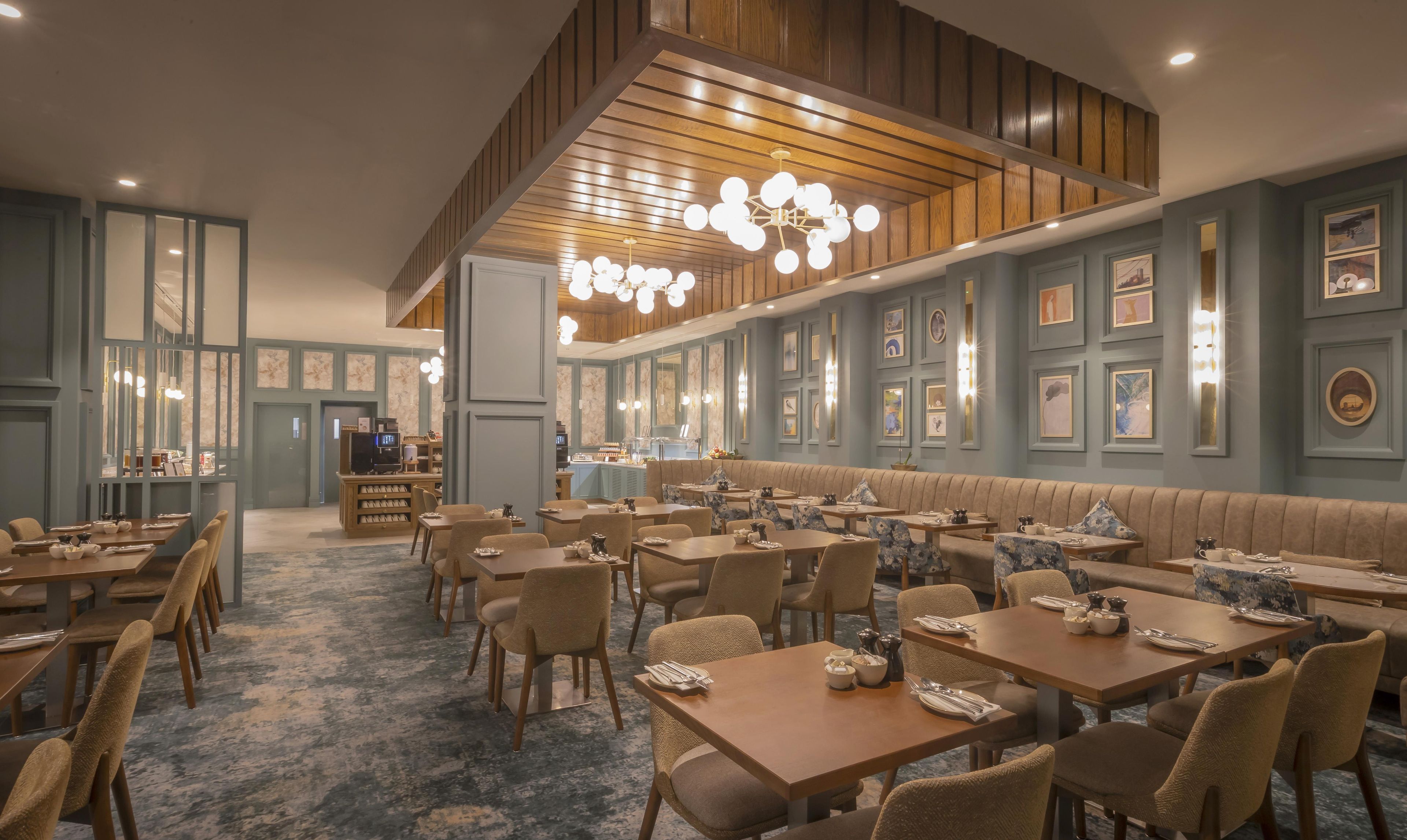En restaurant med flere spiseborde og siddepladser, et barområde samt et loft med træpaneler og hængende lamper.
