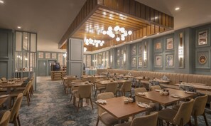 A restaurant with multiple dining tables and booths, a bar area, and a ceiling with wooden paneling and hanging lights. - Hilton Dublin (Dublin)