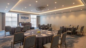 Une salle de conférence équipée de tables rondes, de chaises et d’un grand écran affichant le texte « Hilton Dublin ».