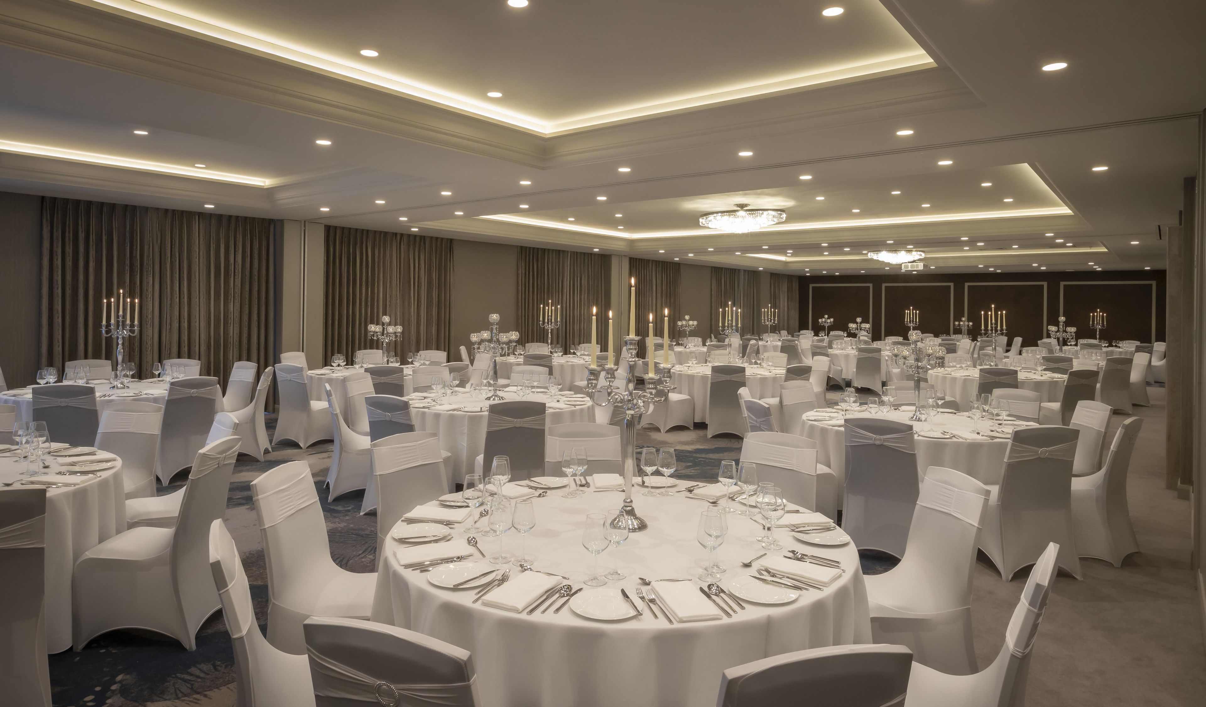 A banquet hall with round tables, white chairs, and chandeliers.