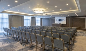 A conference room with rows of chairs, a podium, and a screen displaying 'Hilton Dublin'. - Hilton Dublin (Dublin)