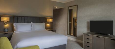 Habitación de hotel con una cama grande, lámparas de noche, televisor de pantalla plana, un espejo y una pequeña zona de estar.