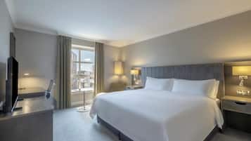 A hotel room with a large bed, a desk, a chair, a TV, and a window with curtains.
