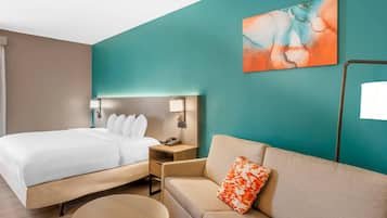 Una habitación de hotel con cama, sofá, mesita de noche, lámpara y un cuadro en la pared.