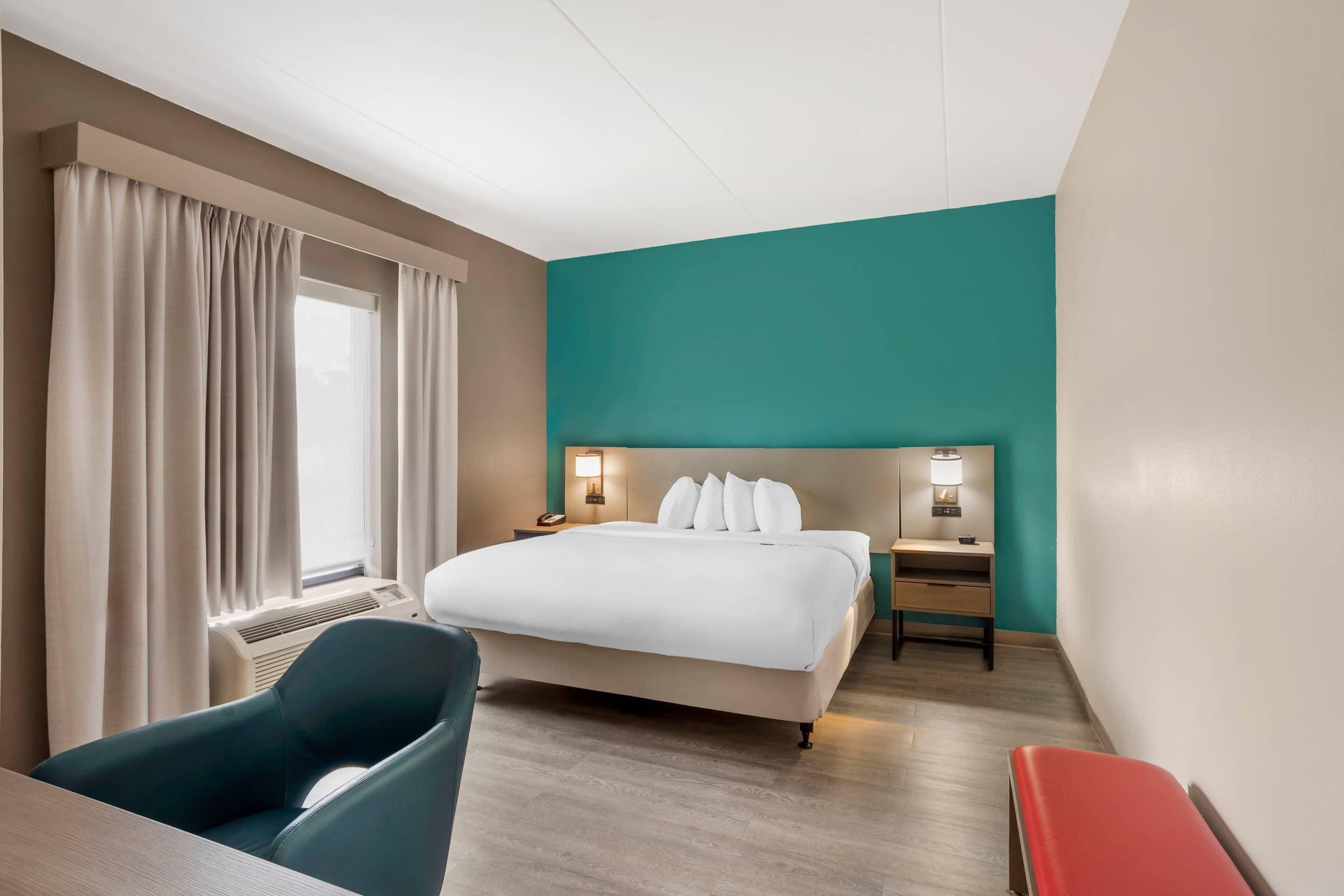 A hotel room with a bed, bedside tables, a desk, a chair, and a window with curtains.