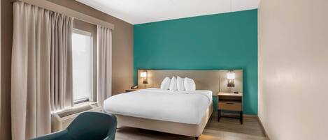 A hotel room with a bed, bedside tables, a desk, a chair, and a window with curtains.
