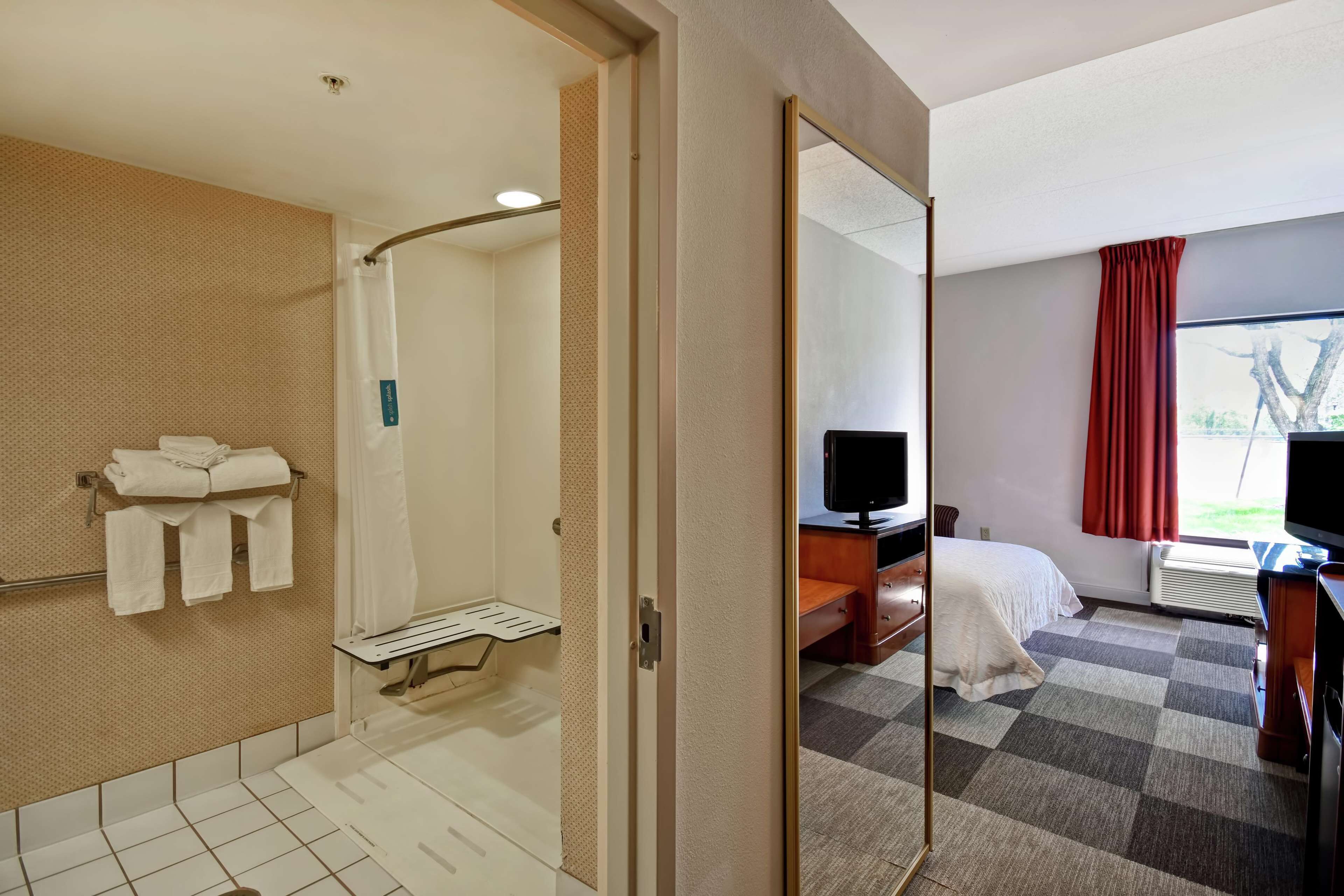 A hotel room with a shower, a bed, a TV, and a desk.