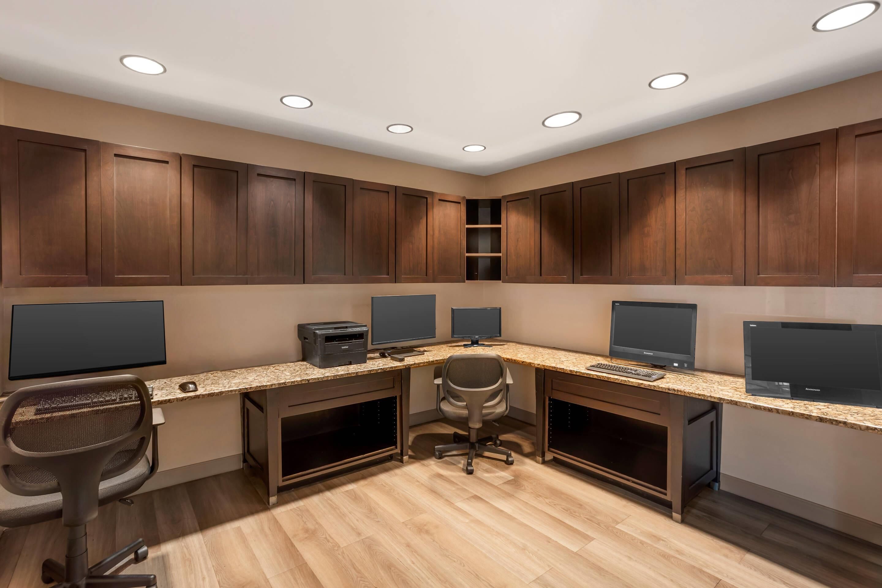 A modern office space with a long desk, two monitors, a printer, and a chair.