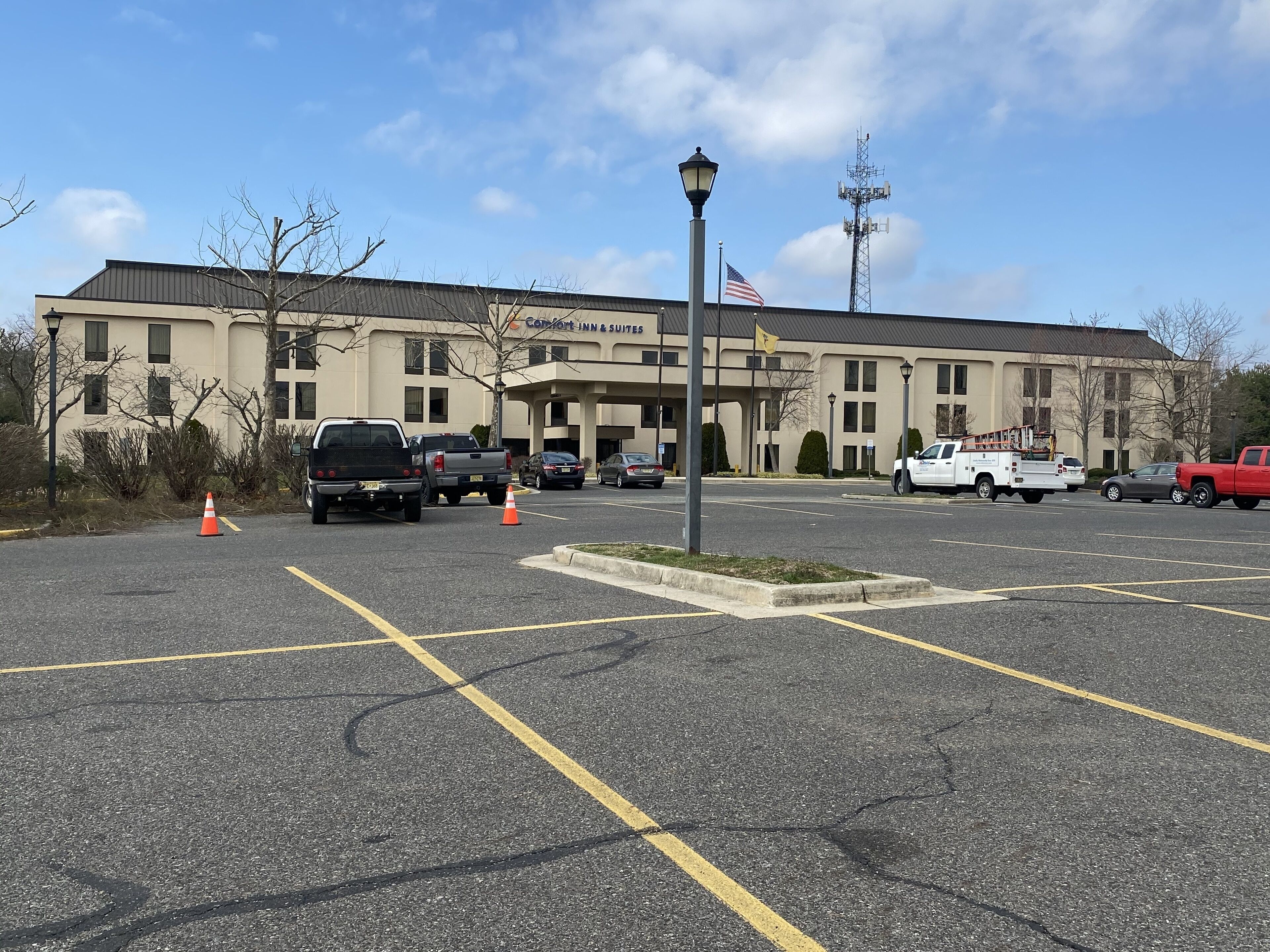 A parking lot in front of a hotel with multiple vehicles, including a white utility truck and a red pickup truck.