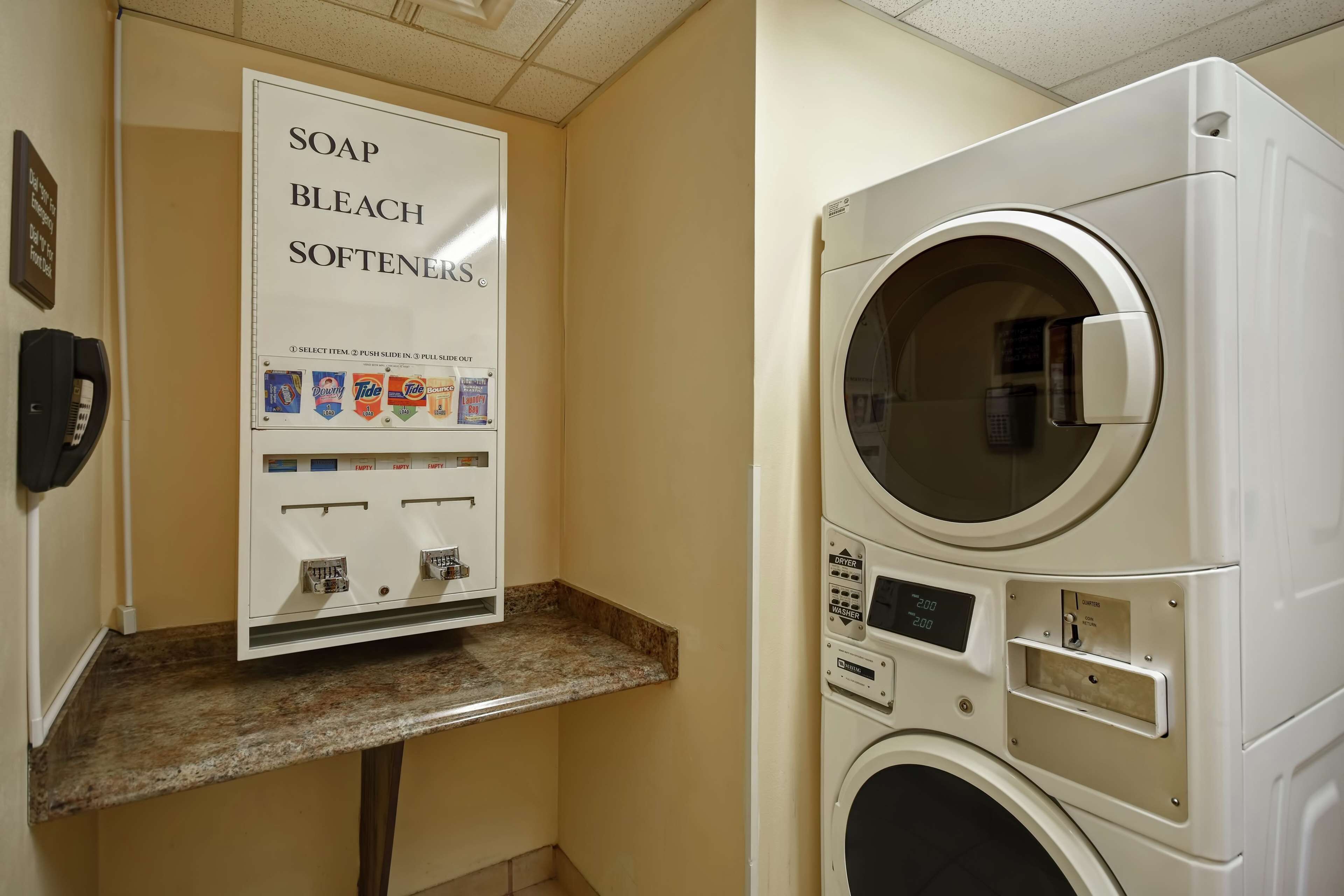 A laundry facility with a soap and bleach softener dispenser and a stacked washer and dryer.