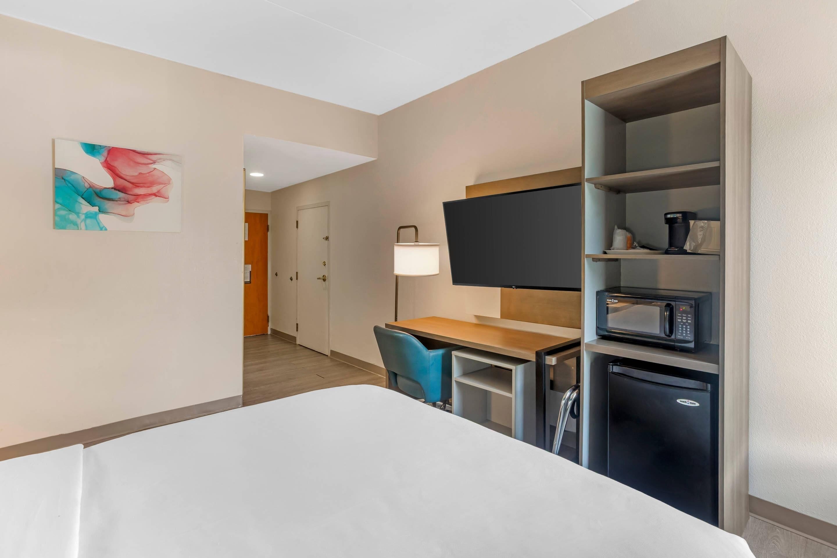 A hotel room with a bed, a desk, a chair, a television, a microwave, and a refrigerator.