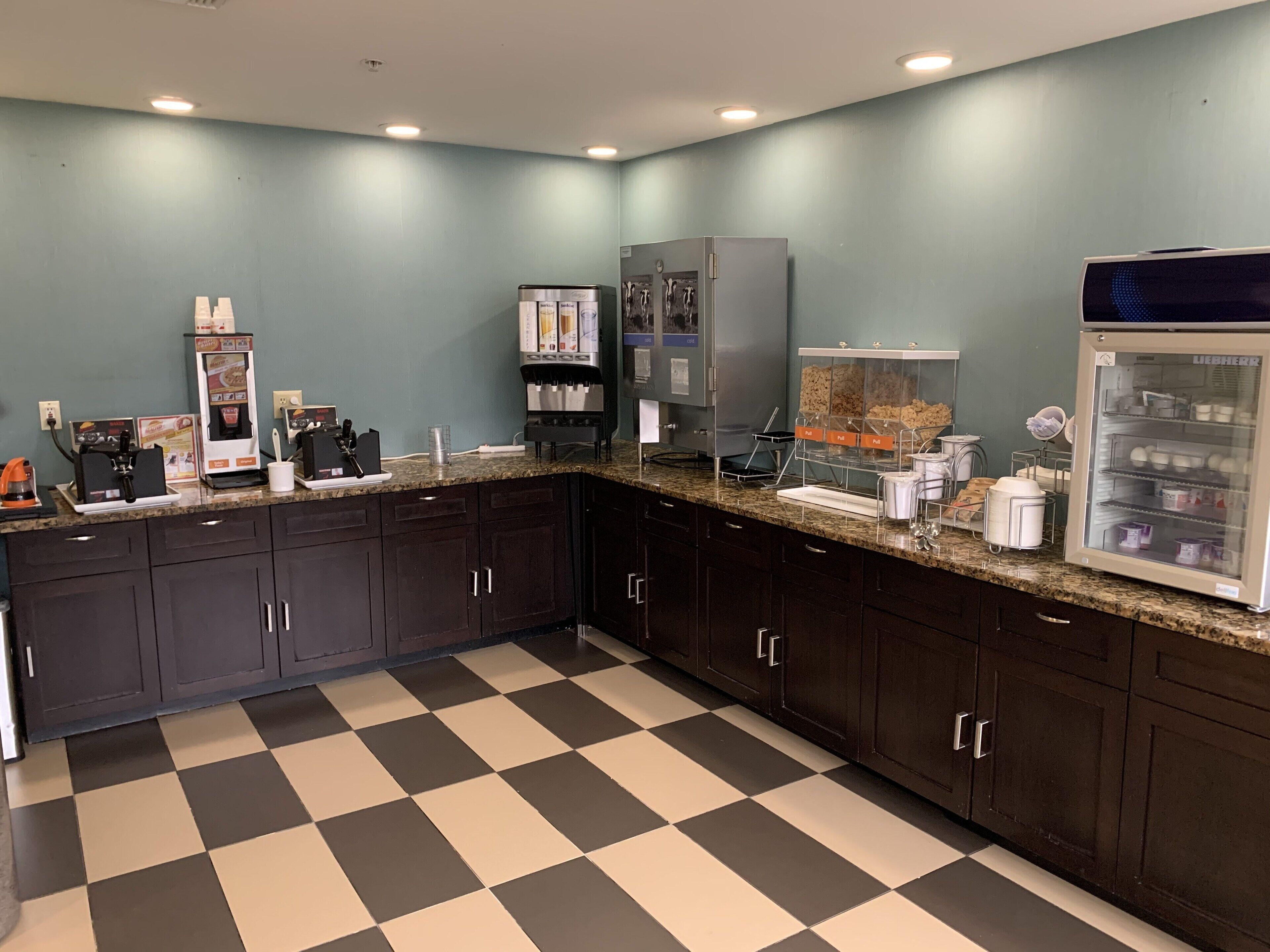 A kitchen area with dark cabinets, a checkered floor, a coffee machine, a refrigerator, and a beverage dispenser.