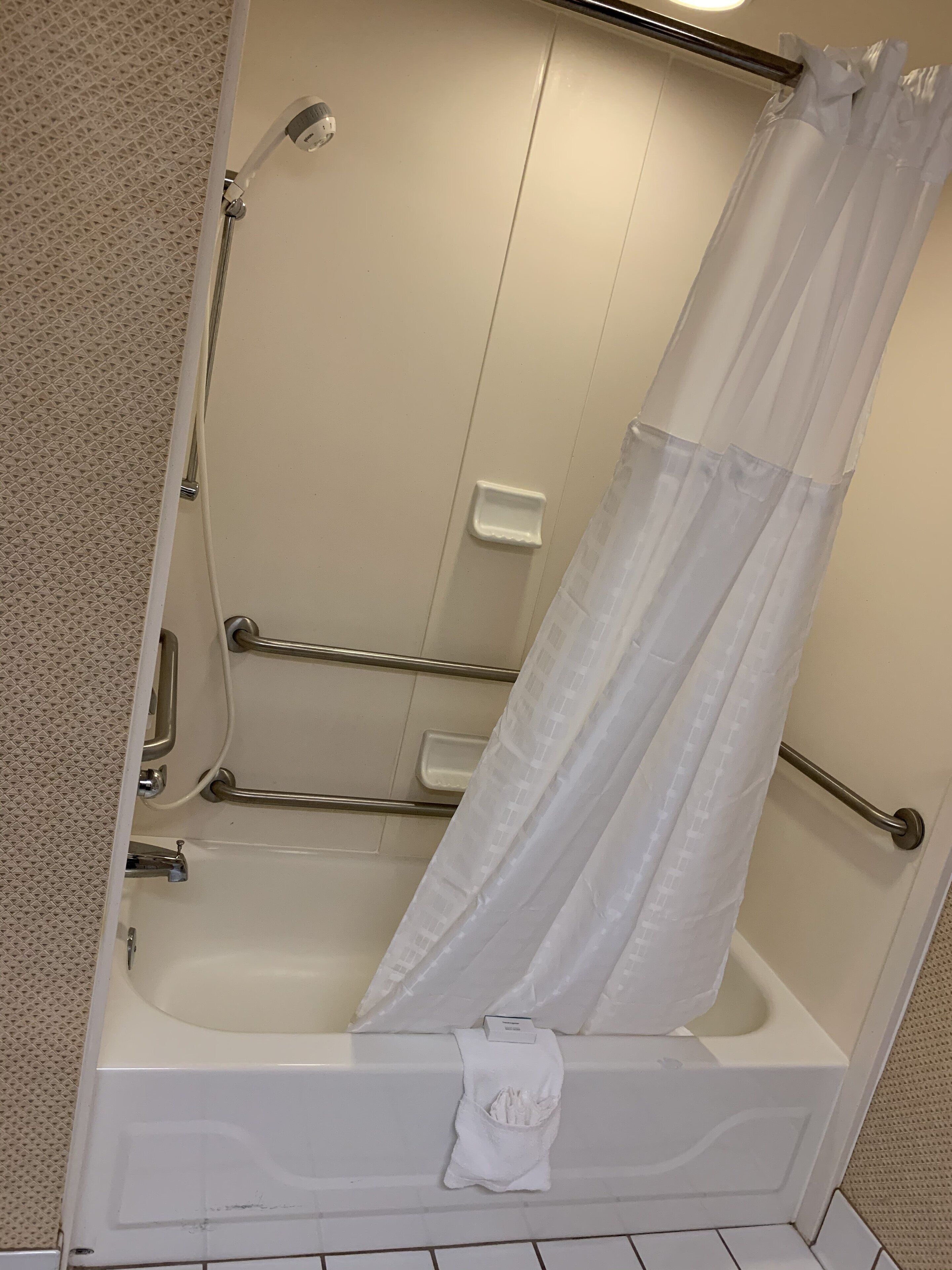 A bathtub with a white shower curtain, a handheld showerhead, and a grab bar.