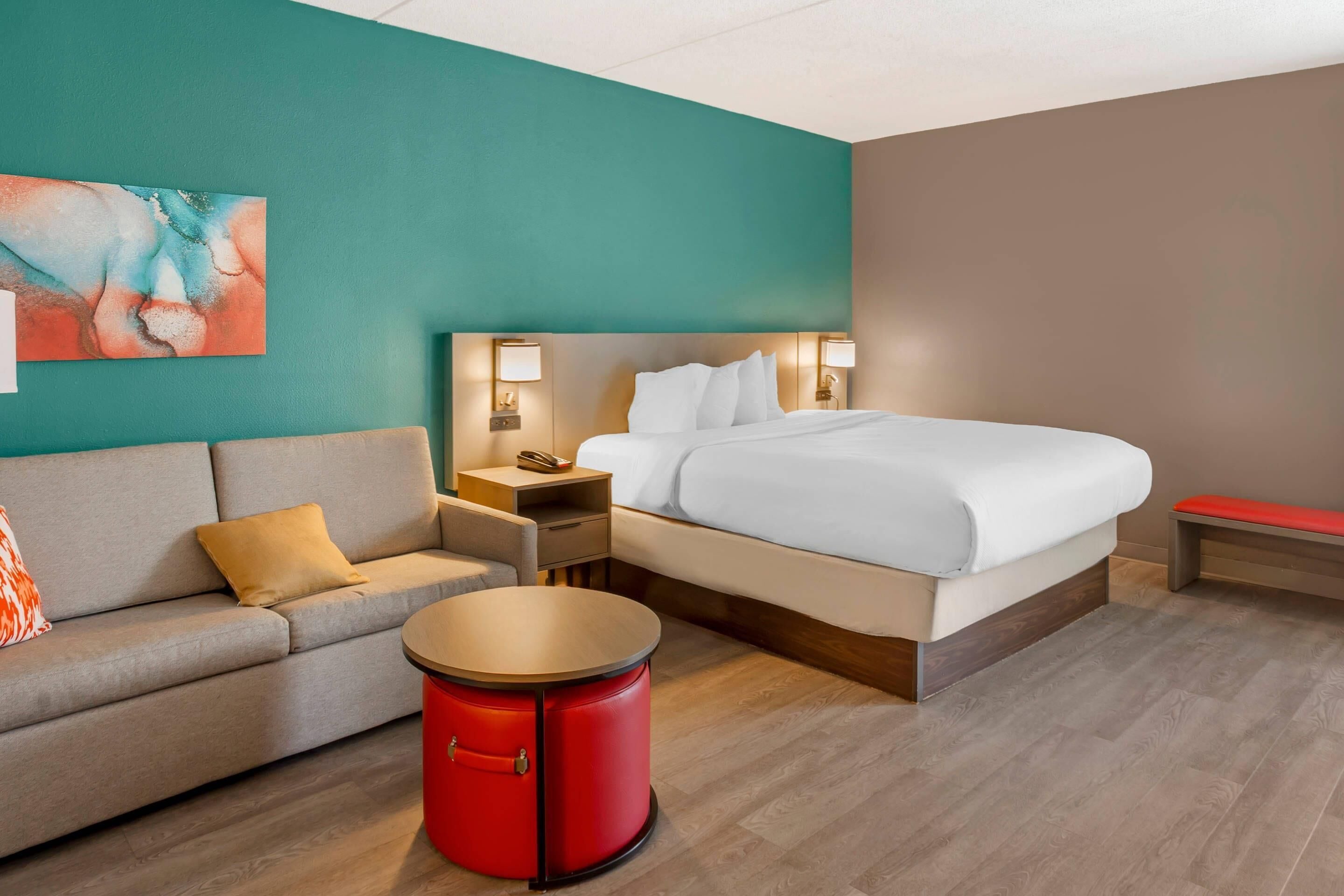 A hotel room with a bed, a sofa, a small table, and a nightstand with a lamp.