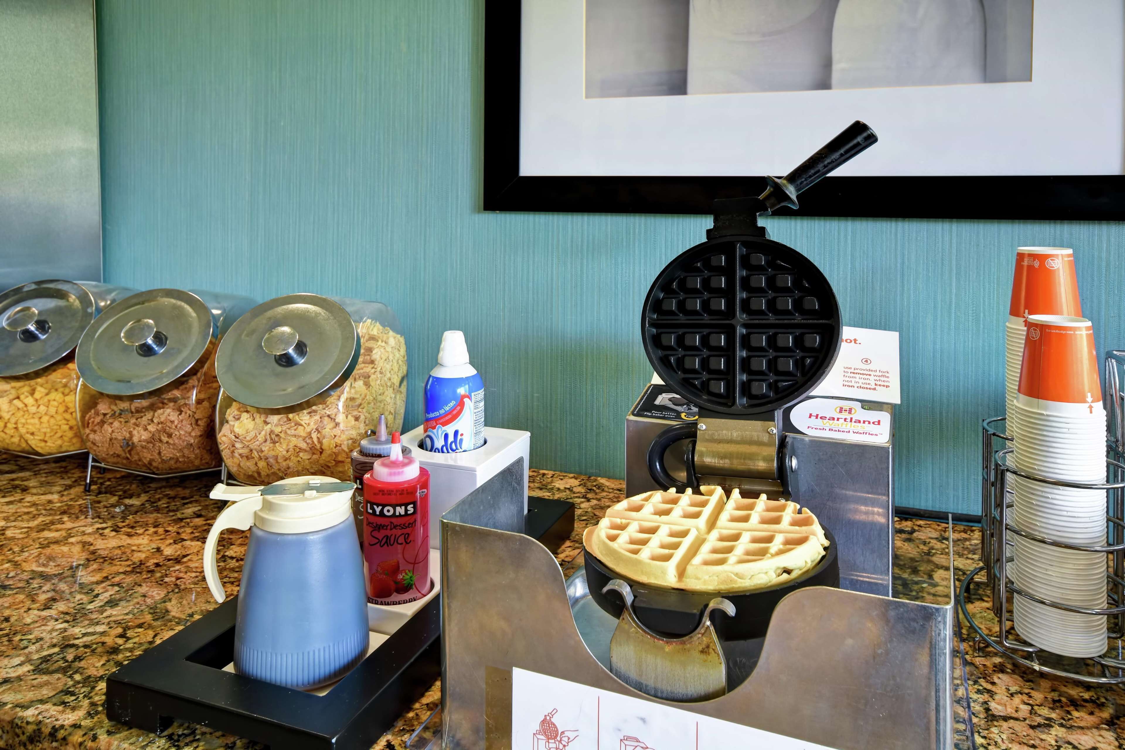 A breakfast buffet setup with waffle irons, condiments, and stacked plates.