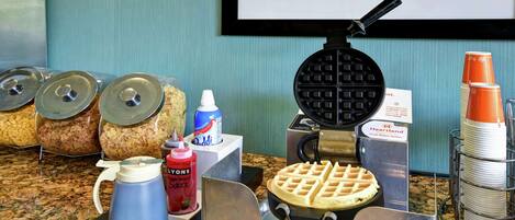 A breakfast buffet setup with waffle irons, condiments, and stacked plates.
