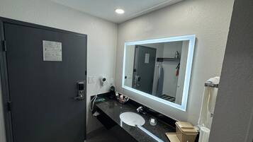 Un baño moderno con puerta oscura, un espejo grande, un lavabo y un perchero para toallas.