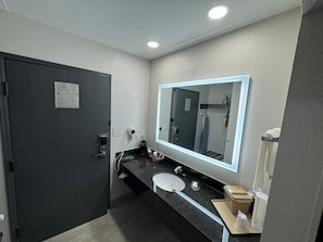 Une salle de bain moderne avec une porte sombre, un grand miroir, un lavabo et un porte-serviettes.
