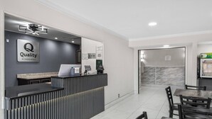 Eine Rezeption mit modernem Design, einem Empfangstresen, einer Theke, einer Kaffeemaschine und einer Sitzecke mit Tischen und Stühlen.