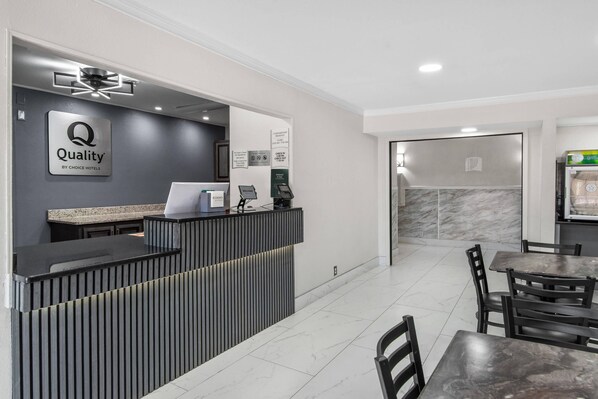 A hotel reception area with a modern design, a reception desk, a counter, a coffee machine, and a seating area with tables and chairs.
