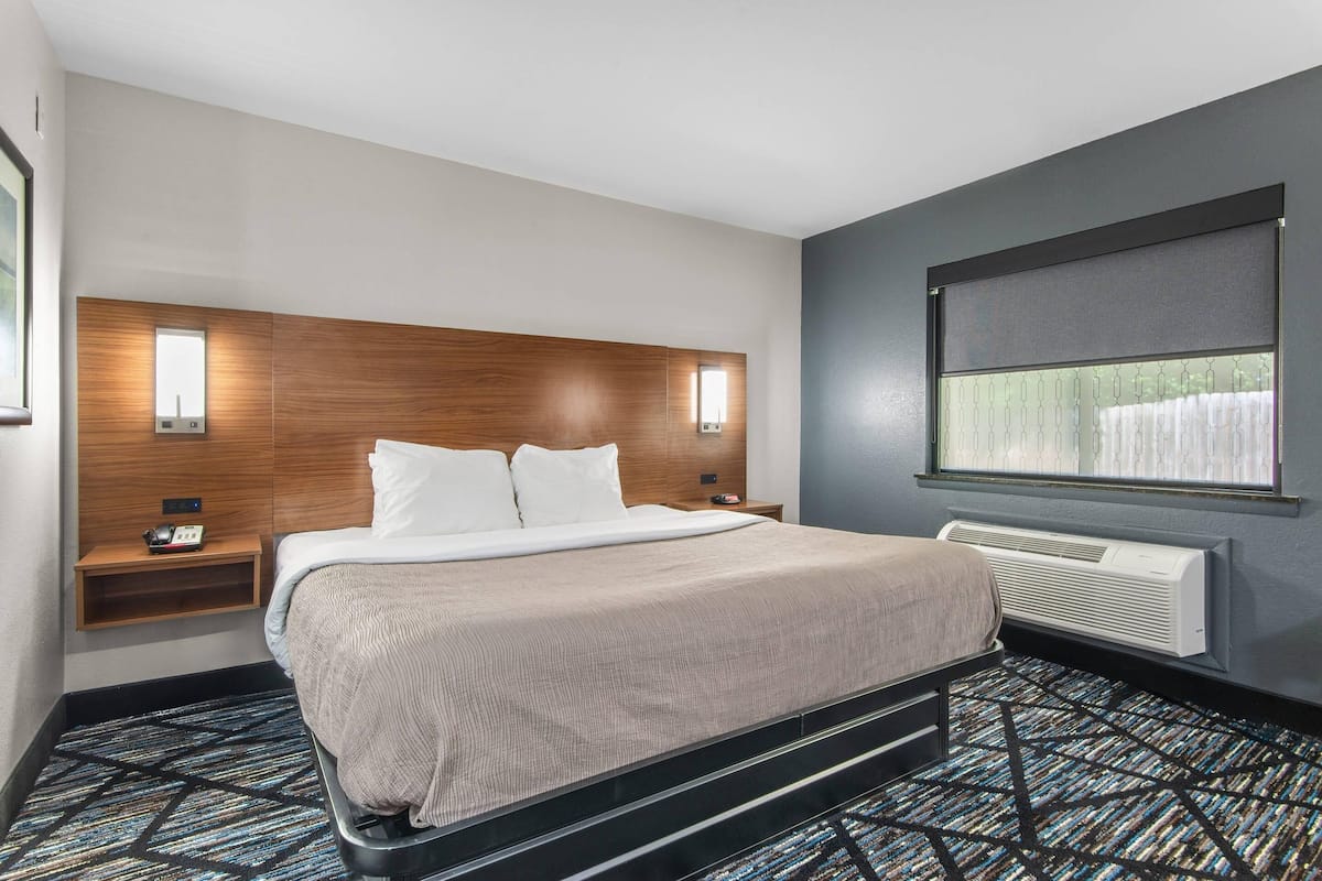 A modern hotel room with a large bed, a nightstand, a wall-mounted heater, and a window with blinds.