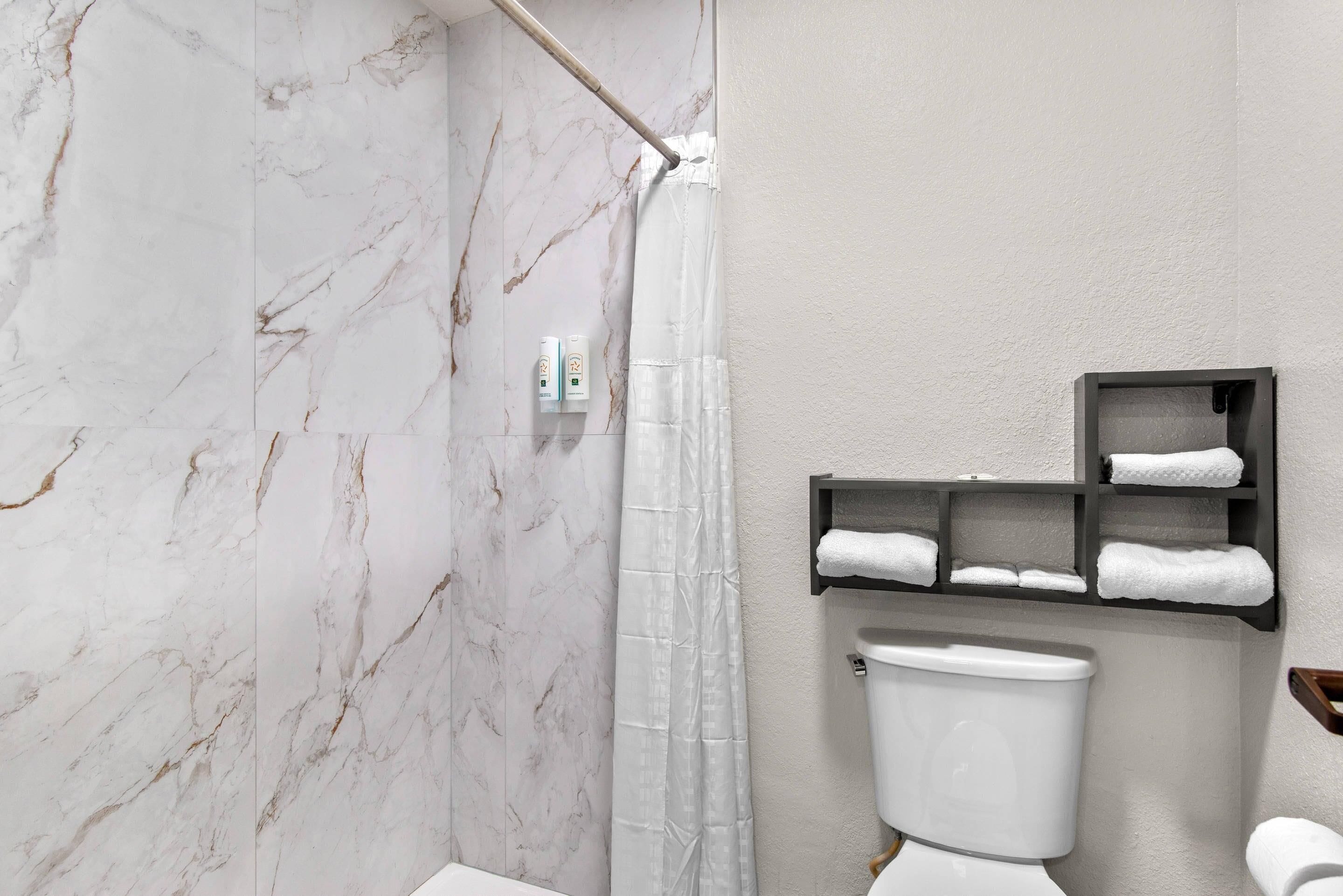 Une salle de bain avec un mur en marbre, un rideau de douche, des toilettes et une étagère avec des serviettes.