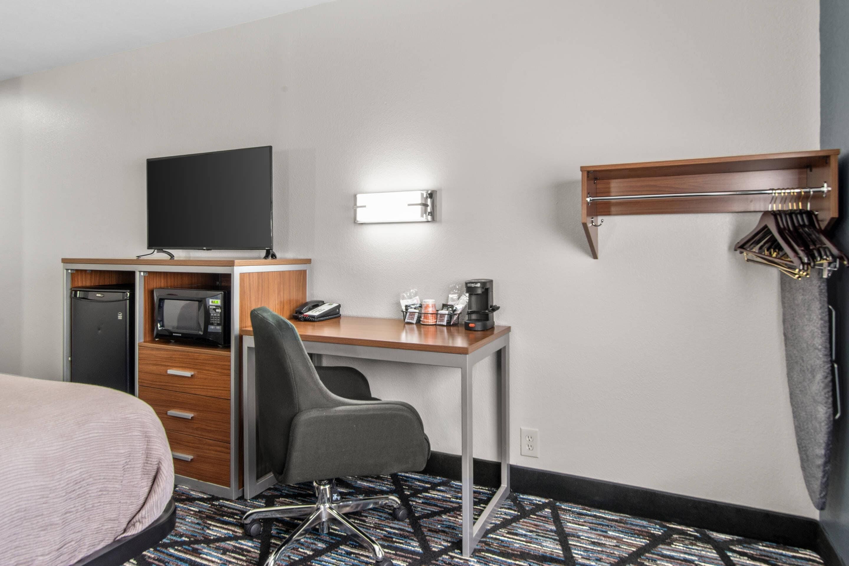 A hotel room with a bed, desk, chair, television, microwave, coffee maker, and a coat rack.