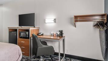 A hotel room with a bed, desk, chair, television, microwave, coffee maker, and a coat rack.