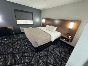 A hotel room with a bed, a desk, a chair, a nightstand, and a wall-mounted TV.