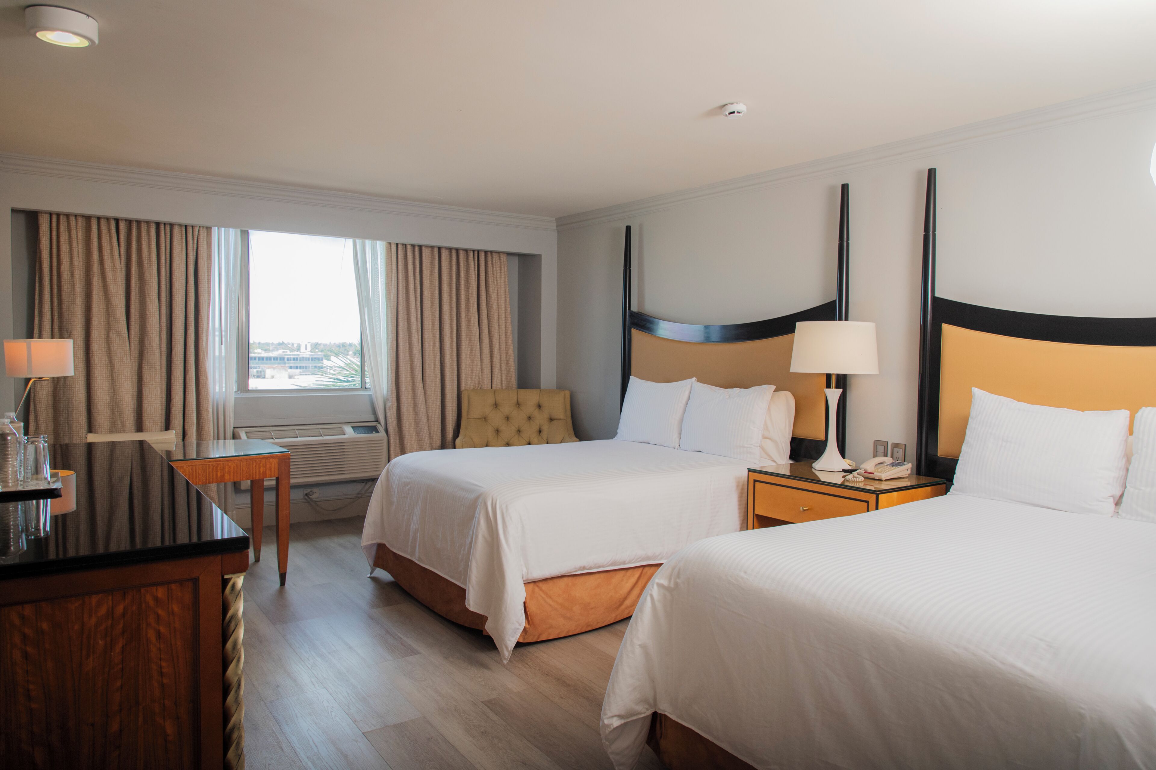 Une chambre d’hôtel avec deux lits, un bureau, une chaise, une lampe et une vue sur la ville.