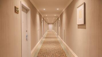 Un pasillo de hotel con suelo alfombrado, puertas a ambos lados y cuadros en las paredes.