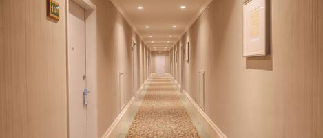 Un pasillo de hotel con suelo alfombrado, puertas a ambos lados y cuadros en las paredes.