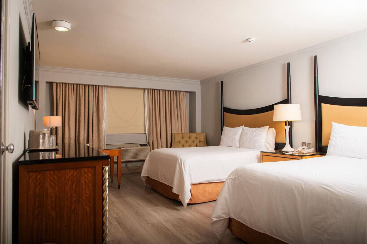 A hotel room with two beds, a desk, a chair, a TV, and a window with curtains.
