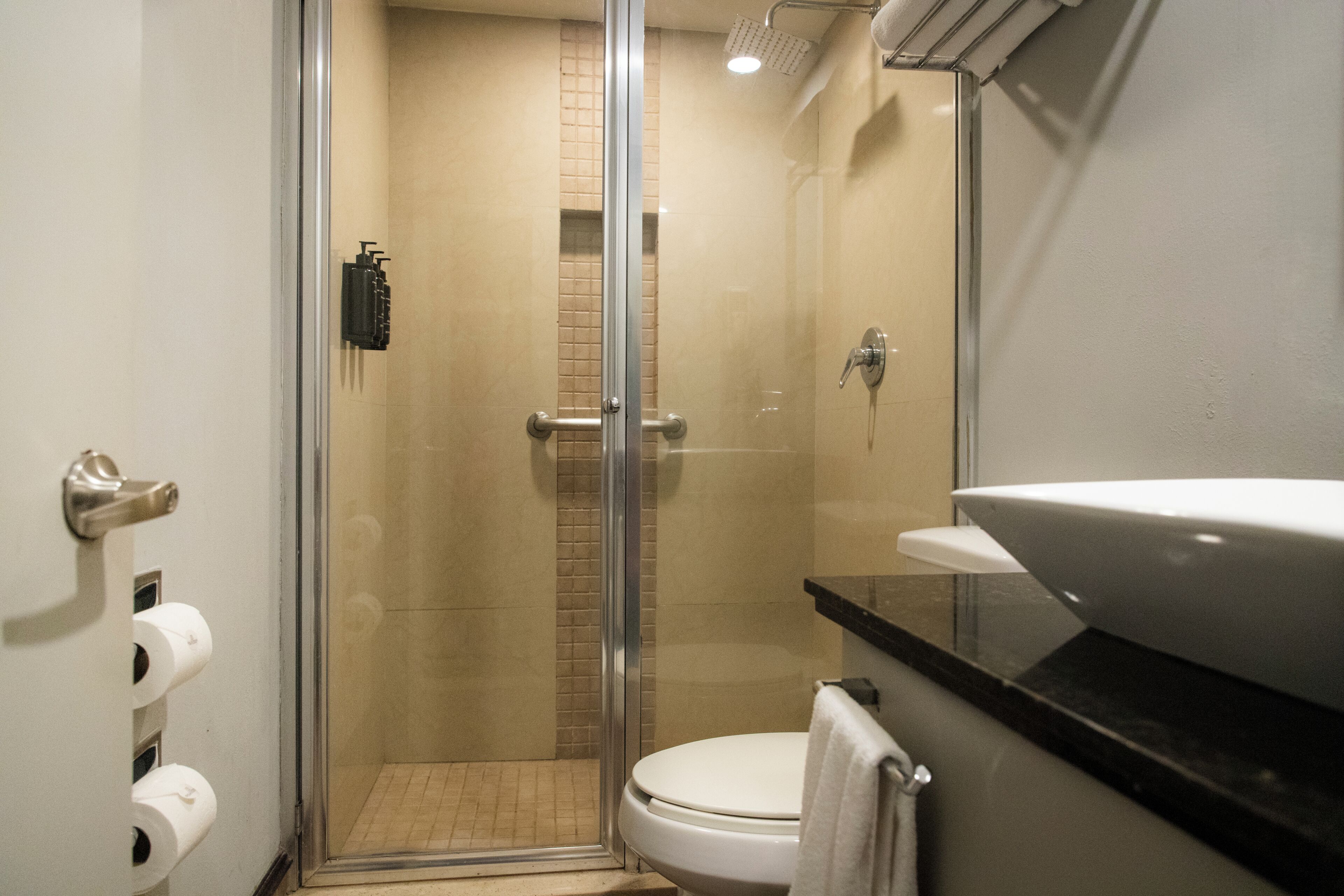 A bathroom with a glass-enclosed shower, a toilet, and a sink with a towel hanging on the wall.
