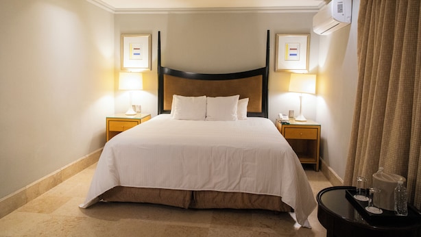 Ein Hotelzimmer mit einem großen Bett, Nachttischlampen, einem Nachttisch und einer Klimaanlage.