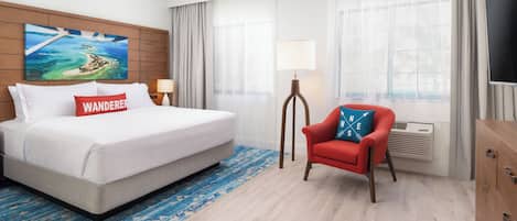 A hotel room with a large bed, a red armchair, a television, and a painting of a coastal landscape.
